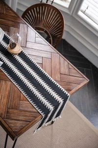 Détail d'un chemin de table bohème rayé noir et blanc avec glands sur une table en bois