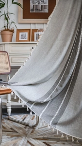 Close-up detail of linen curtain texture with white tassels and dark grey stripes