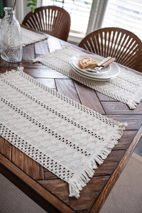 Macro detail of hand-woven off-white cotton table runner with geometric textures and tassels