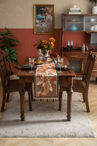 Detailed close-up of orange floral table runner with tassel decor on a wooden dining table