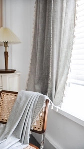 Close-up of linen-textured grey curtain featuring white tassel trim and rustic boho style