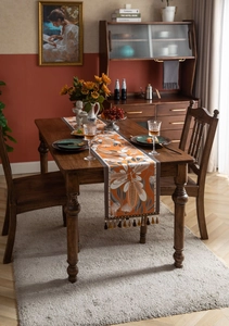 Detail of orange tropical leaf table runner with decorative fringe on dark wood table