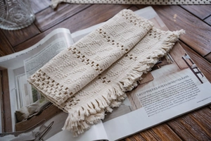 Close-up of cream cotton table runner featuring geometric crochet texture and long fringe