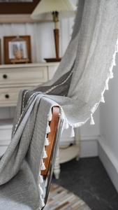 Close-up of grey linen textured curtain fabric featuring decorative white cotton tassels