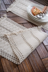Close-up of bohemian hand-woven cream table runner with geometric textures and tassels