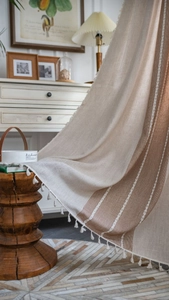 Detail of bohemian linen curtain featuring brown stripes and decorative white tassels