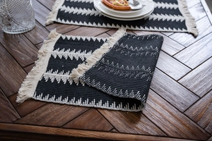 Détail d'un chemin de table tissé noir et blanc avec franges sur une table en bois
