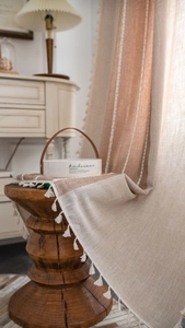 Detail showing linen curtain with brown stripes and white tassel trim on wood stool