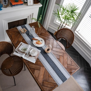 Gray and blue striped woven table runner with decorative tassels on a rustic wood table