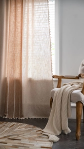 Detail of linen texture curtain with elegant tassel trim and a warm camel beige patchwork design