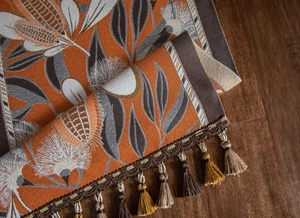 Detailed view of jacquard table runner with orange leaf pattern and handmade tassels
