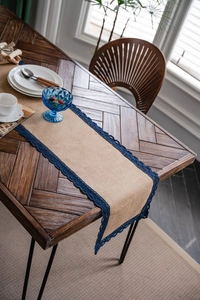 Detail van natuurlijke jute tafelloper met donkerblauwe kanten rand op houten tafel