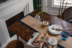 Detail van natuurlijke jute tafelloper met marineblauwe kanten rand op houten tafel
