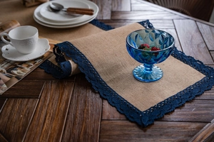 Detail van natuurlijke jute tafelloper met donkerblauwe gehaakte kant op houten tafel