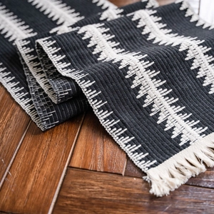 Chemin de table tissé noir et blanc avec motifs géométriques et pompons blancs