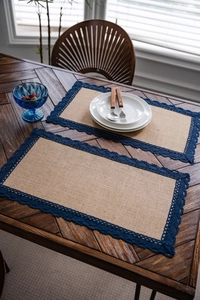 Detail van natuurlijke jute placemats met donkerblauwe kant op een rustieke houten eettafel