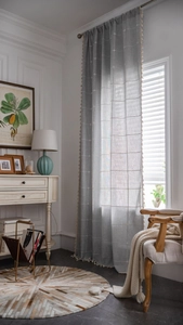Close-up of grey plaid semi-sheer curtain with beige tassel balls in farmhouse style
