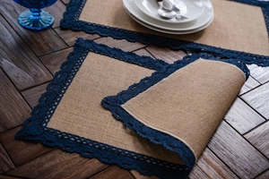 Detail van natuurlijke jute placemat met donkerblauwe gehaakte kant op houten tafel