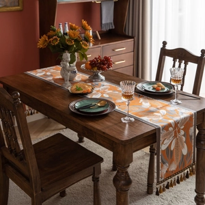 Bohemian jacquard table runner with orange floral pattern and tassels on dark wood table
