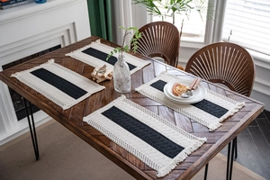 Close-up of four woven cotton placemats with black stripes and fringed edges on wood table