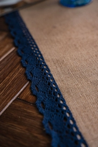 Detail van natuurlijke jute tafelloper met marineblauwe kant op een rustieke houten tafel