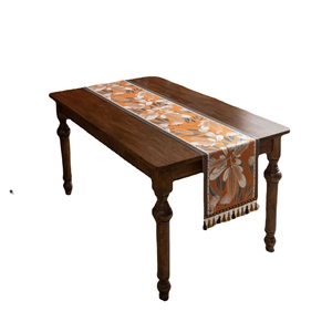 Artistic jacquard table runner with orange floral pattern and tassels on wood table