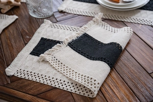 Close-up of black and white woven table runner with tassel fringe on wood table