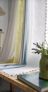 Detail of linen texture curtain with striped patchwork, tassel trim, and geometric embroidery