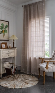 Detail of linen texture beige curtains with white grid patterns and fringe tassels
