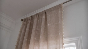 Detailed close-up of light brown linen farmhouse curtains with white plaid and tassel trim