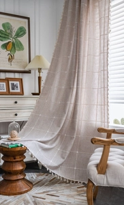 Detail showing beige plaid pattern fabric with elegant white tassel trim and linen texture