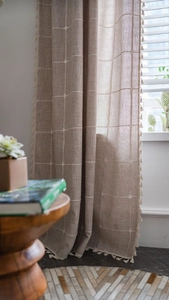 Close-up of linen-textured curtain featuring white grid patterns and fringe trim details