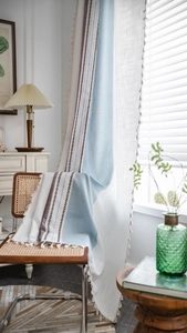 Gros plan sur les rideaux en patchwork bleu et beige avec franges et détails tissés