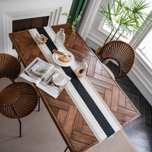 Minimalist black and white woven table runner with tassels on a rustic wooden dining table