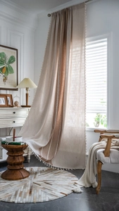 Detail of boho beige linen curtain with striped patchwork and white ball fringe tassels