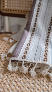 Detail of bohemian striped embroidery and white cotton tassels on linen fabric
