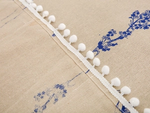 Detailed close-up of blue floral cotton linen fabric with soft white pom-pom fringe trim