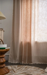 Detail of linen curtains with vertical stripes and delicate beige tassel fringe