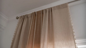 Detail of beige and brown linen curtains with embroidery stripes and tassel fringe