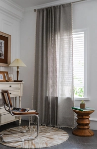 Detail showing grey linen texture curtains with vertical stripes and white fringe tassels