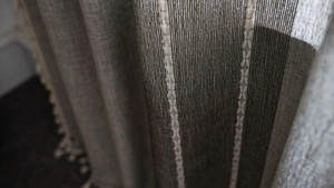 Detail of coarse textured curtain with white X-embroidery and ivory pompom tassels