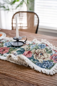 Detail of vintage floral jacquard table runner with delicate cream tassels on a wood table
