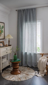 Détail de rideau en lin bleu-gris avec broderie rayée blanche et glands de couleur crème