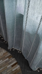 Detail view of light blue linen curtain with white leaf embroidery and tassel trim