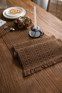 Detail of dark brown crochet table runner with hollow flowers and fringe on wood table
