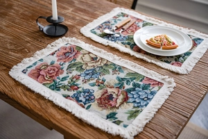 Detailed close-up of floral jacquard place mats with fringe edges on wooden table