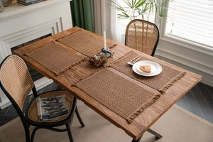 Macro detail of four woven brown place mats with fringe on a wooden dining table