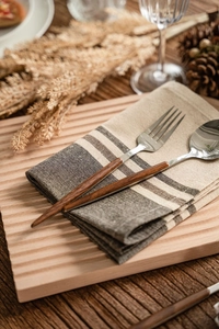 Detail of stainless steel cutlery with wood handles on a striped linen napkin