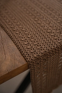 Macro shot of dark coffee woven table runner with hollow floral pattern on wood