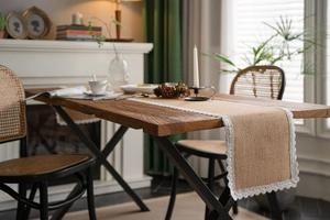 Detailed view of burlap table runner with white lace trim on a rustic wooden table surface